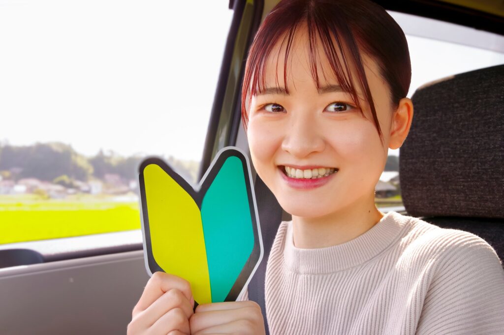 運転席で初心者マークを持って笑顔の若い女性