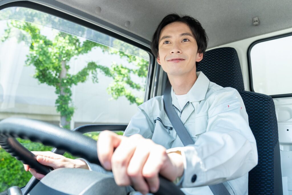 トラックの運転席でハンドルを握る笑顔の若いドライバー